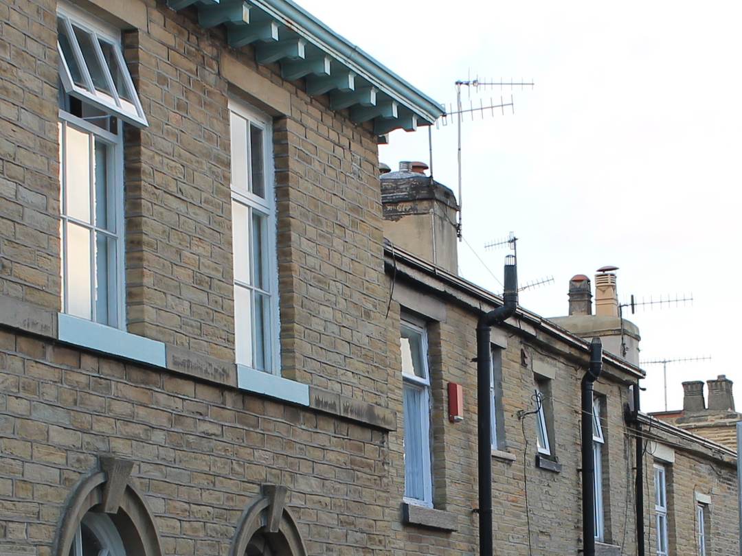 Stone terraced houses stepping up a hillside street, with chimney stacks and aerials along the roofline